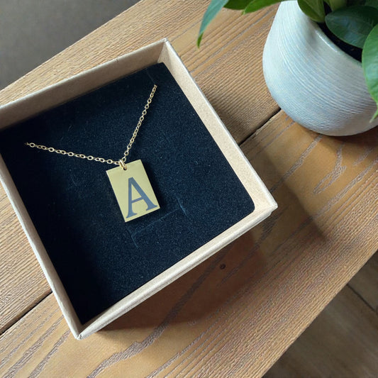 Necklace with a pendant featuring the letter 'A' in a box on a wooden surface.